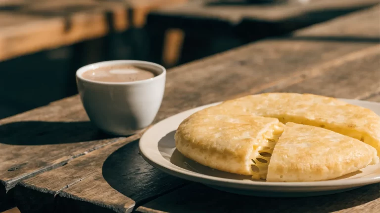 Mbeju de almidón y queso cortado en porciones junto a una taza de cocido