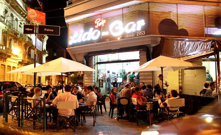Fachada de Lido Bar de noche, con su cartel «desde 1953» y las mesas en la vereda, en el Centro de Asunción