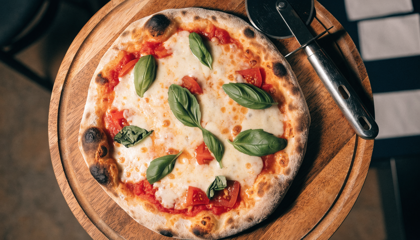 Pizza artesanal recién salida del horno de leña con muzzarella y albahaca sobre tabla de madera. Imagen ilustrativa: no corresponde al local.