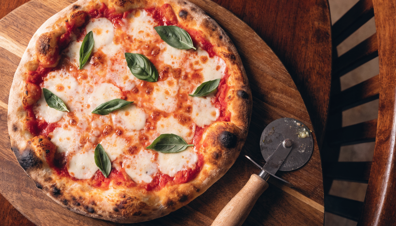 Pizza artesanal recién salida del horno de leña con muzzarella y albahaca sobre tabla de madera. Imagen ilustrativa: no corresponde al local.