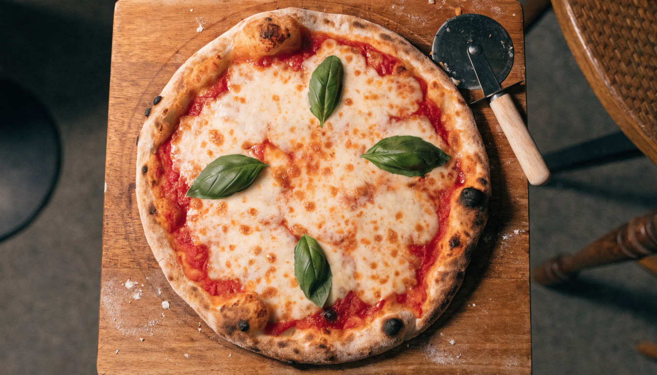 Pizza artesanal recién salida del horno de leña con muzzarella y albahaca sobre tabla de madera. Imagen ilustrativa: no corresponde al local.